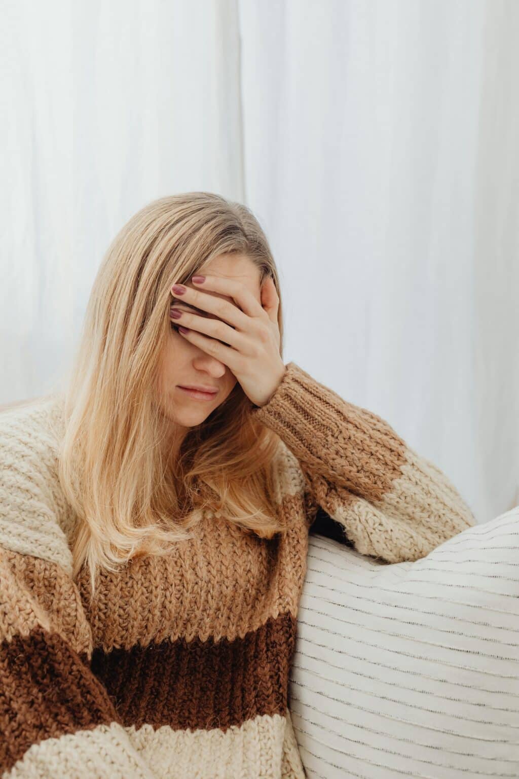 Femme fatigué assis sur un canapé avec la main gauche sur le visage.